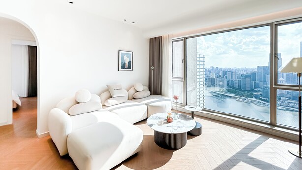 A modern living room with a white sofa, a round coffee table, and a large window with a city view. - Book and Bed-Weifang Store (Shanghai)