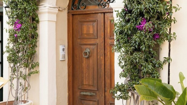 A building entrance with a wooden door, a number '100' sign above it, and large potted plants on either side. - Royal View Suite - Corfu Town (Corfu)