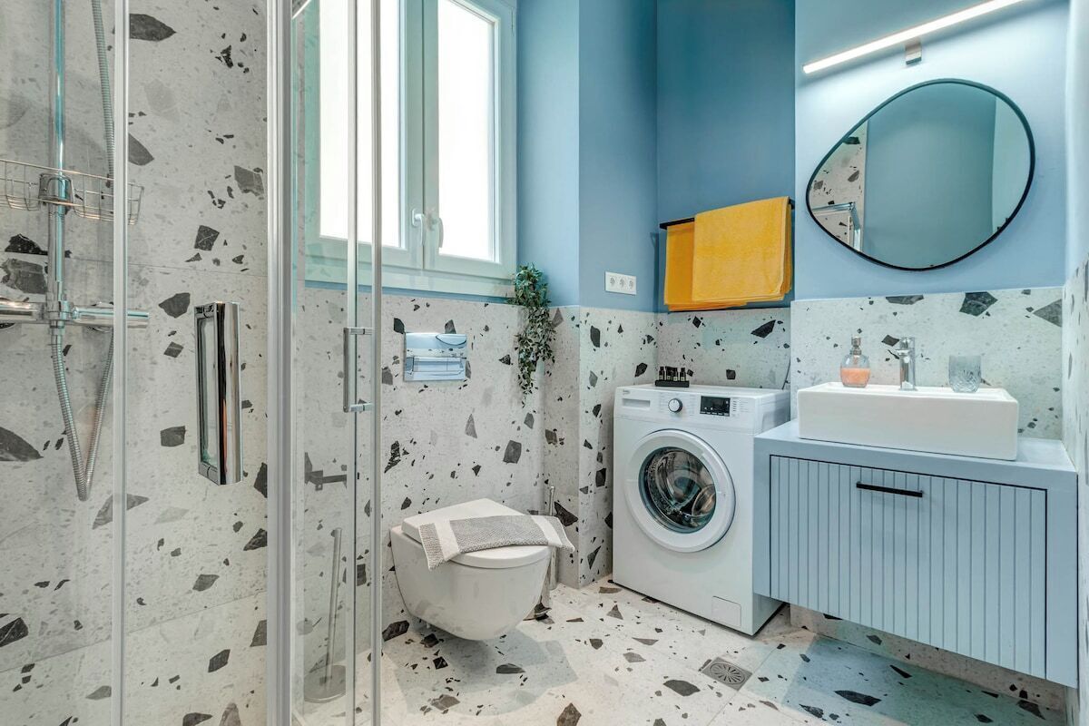 A modern bathroom with a glass shower enclosure, a washing machine, and a sink with a mirror.