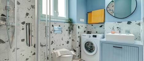 A modern bathroom with a glass shower enclosure, a washing machine, and a sink with a mirror.