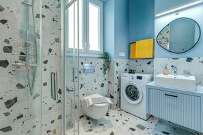 A bathroom with a glass shower enclosure, a washing machine, a sink, and a mirror on the wall. - Royal View Suite - Corfu Town (Corfu)