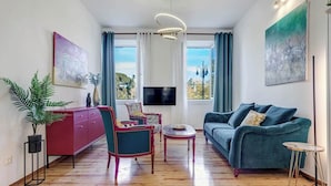 A modern living room with a sofa, chairs, a TV, and a view of the outdoors. - Royal View Suite - Corfu Town (Corfu)