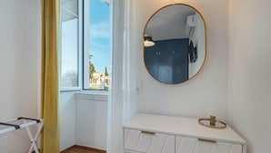 A room with a white vanity, a round mirror, and a window with a view of buildings. - Royal View Suite - Corfu Town (Corfu)