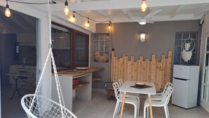 A modern kitchen with a dining area, including a white table and chairs, a hanging chair, and a wooden partition. - The Colibri, Orient Bay, Private Jacuzzi (ST MARTIN)