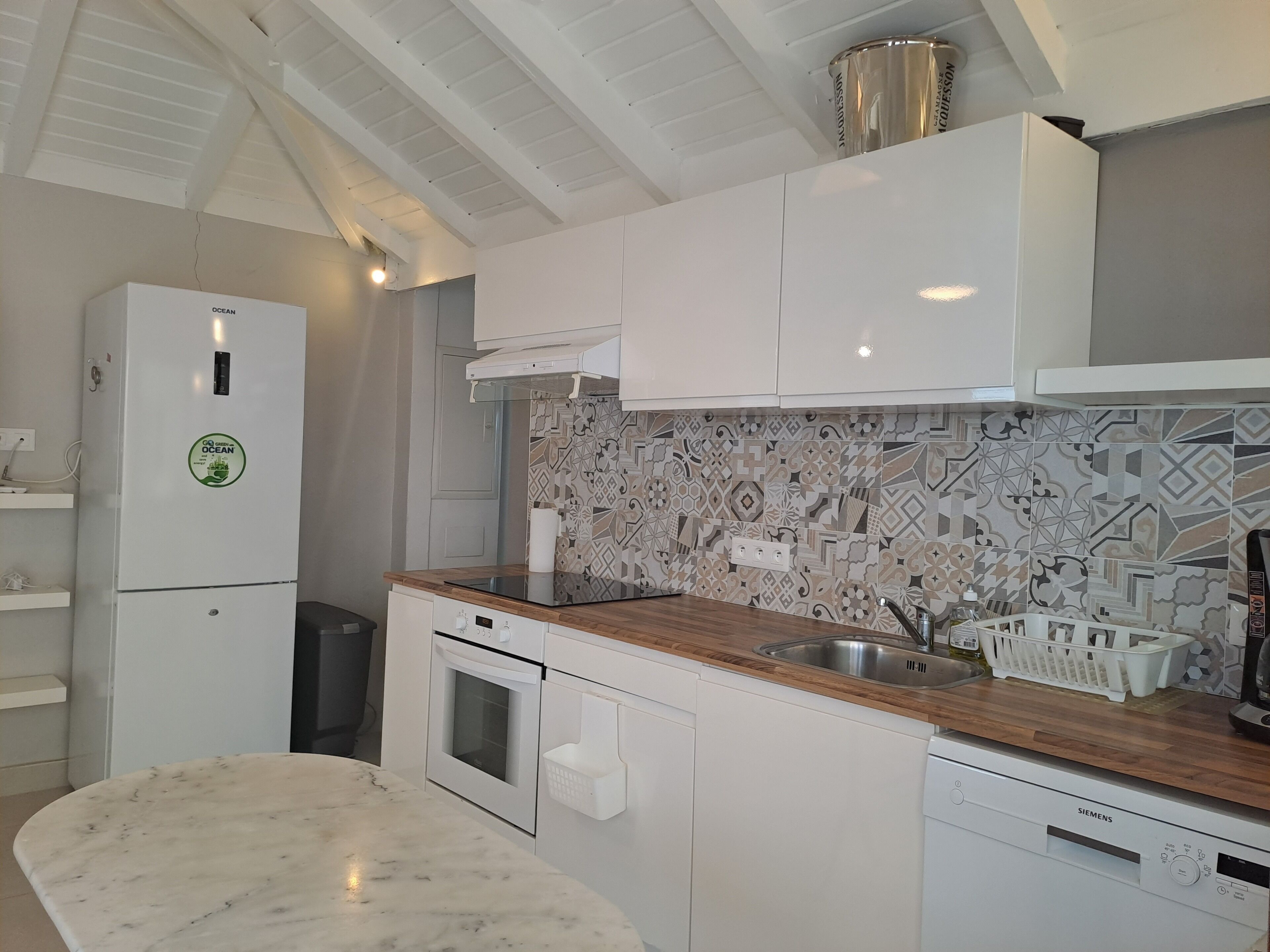 Una cocina moderna con armarios blancos, un salpicadero estampado, encimera de mármol y horno empotrado.