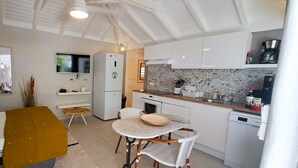 A compact living space with a bed, a dining table, a kitchen area with a microwave, and a TV mounted on the wall. - The Colibri, Orient Bay, Private Jacuzzi (ST MARTIN)