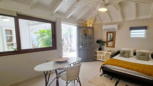 A bedroom with a bed, a small table, and chairs, a window, and a door leading to a balcony. - The Colibri, Orient Bay, Private Jacuzzi (ST MARTIN)