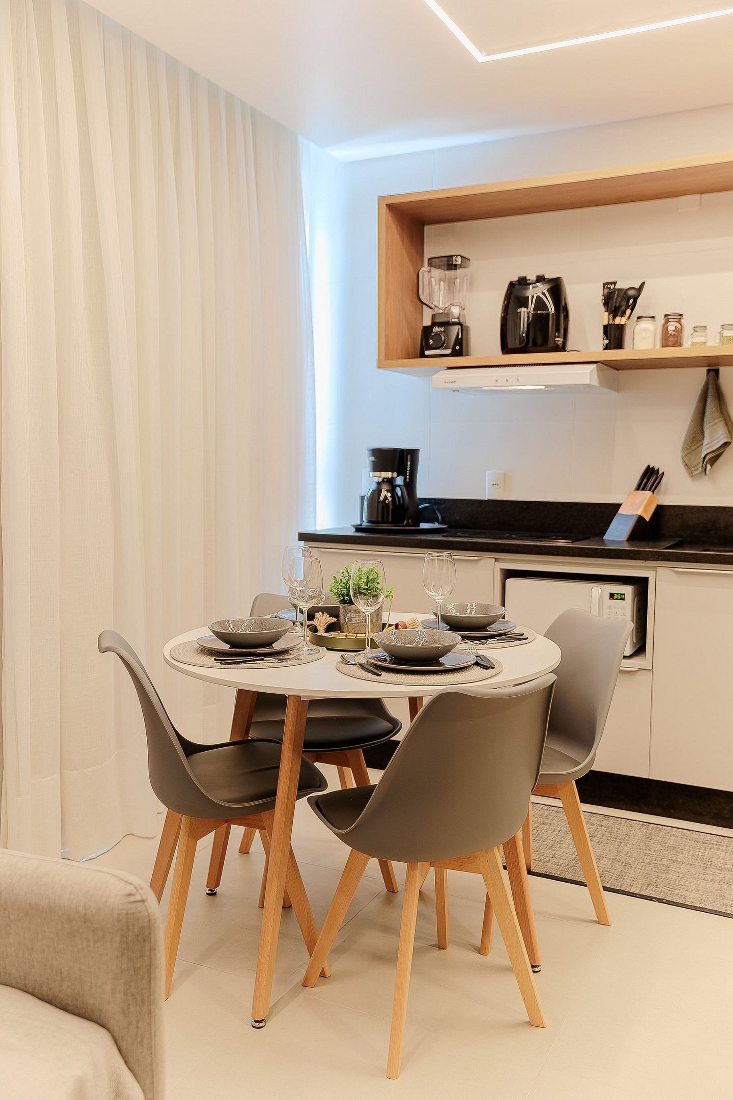 A modern kitchen with a dining area, featuring a round table with chairs, a coffee machine, and a built-in oven.