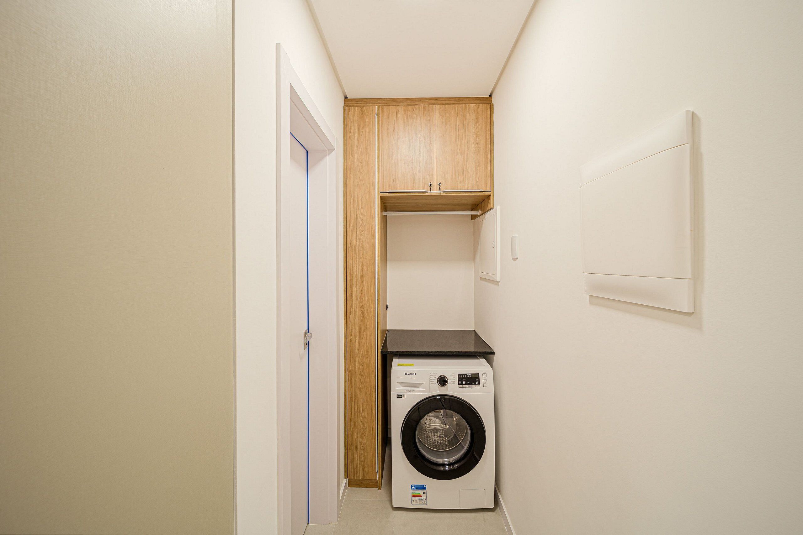 A laundry room with a washing machine, a wooden cabinet, and a door.