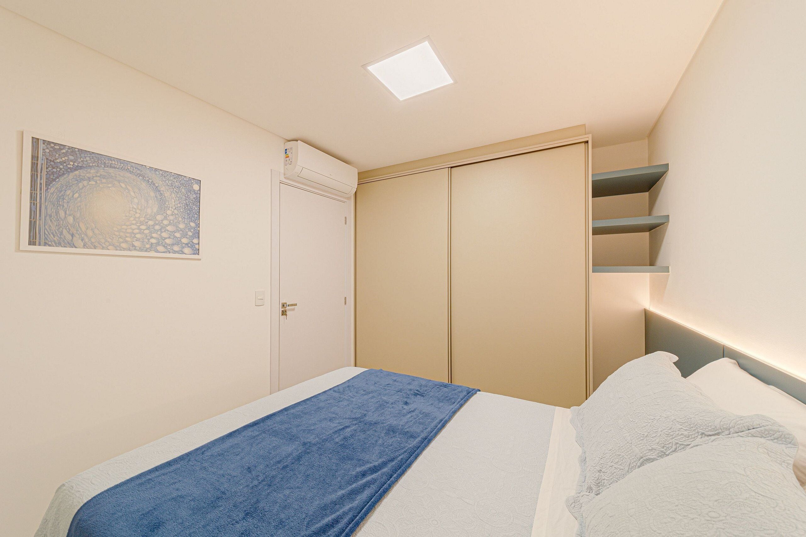 A bedroom with a bed, a blue towel, a white pillow, a closet, and a wall-mounted shelf.