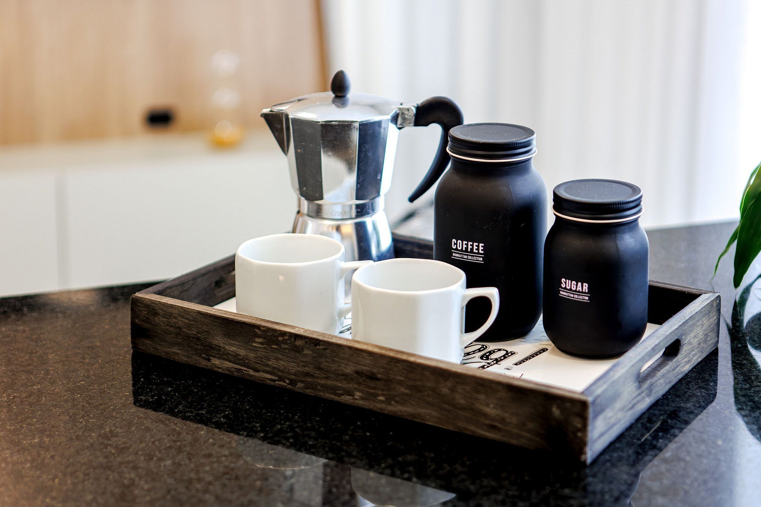 A tray with a coffee maker, two coffee mugs, and two sugar containers on a kitchen counter.