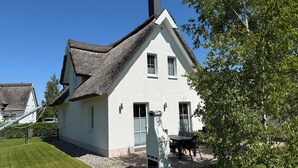 A white house with a thatched roof, a small garden, and a paved driveway.
