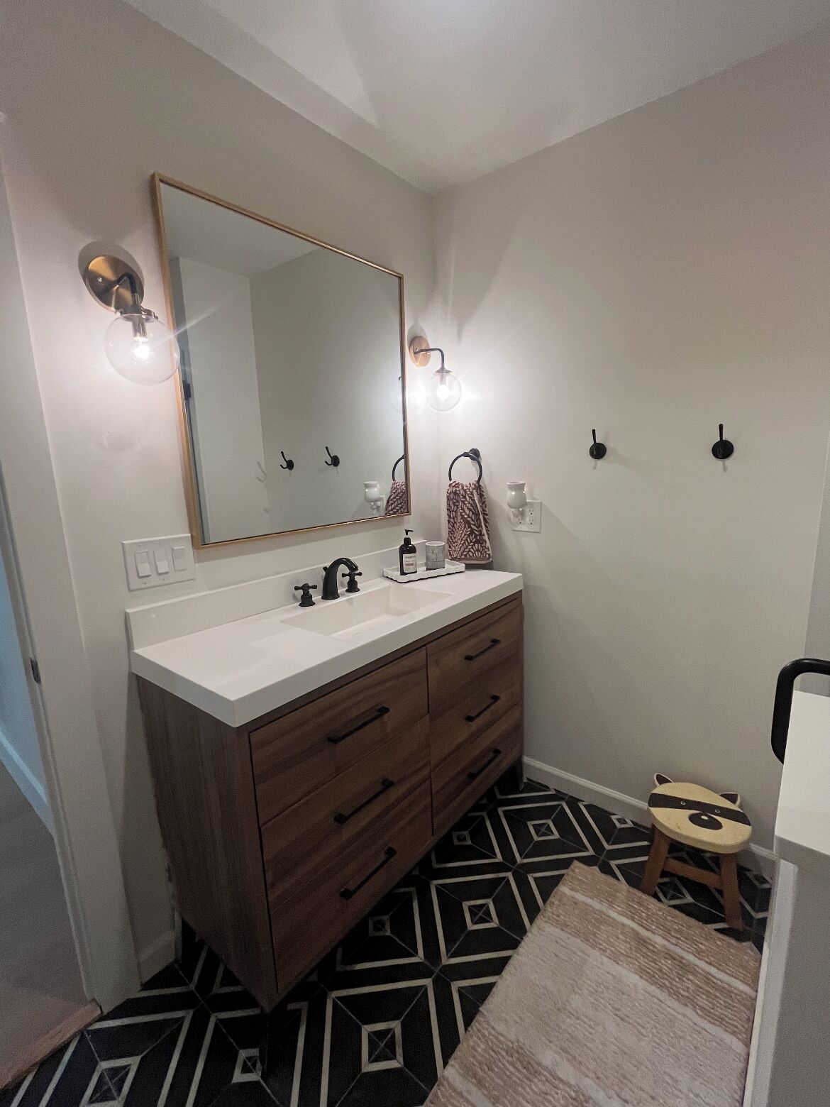 A bathroom with a white vanity, a large mirror, and a geometric patterned floor.
