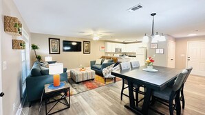 Un salon moderne avec un canapé, un pouf et une table à manger. Il y a également un coin cuisine équipé de placards et d’un four à micro-ondes.