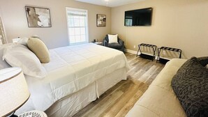 Une chambre à coucher avec un grand lit, un canapé, un fauteuil, une télévision et un ventilateur de plafond.