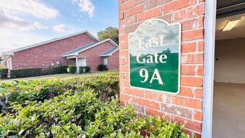 A sign for 'East Gate 9A' on a brick wall, with a building in the background and well-maintained bushes in the foreground.