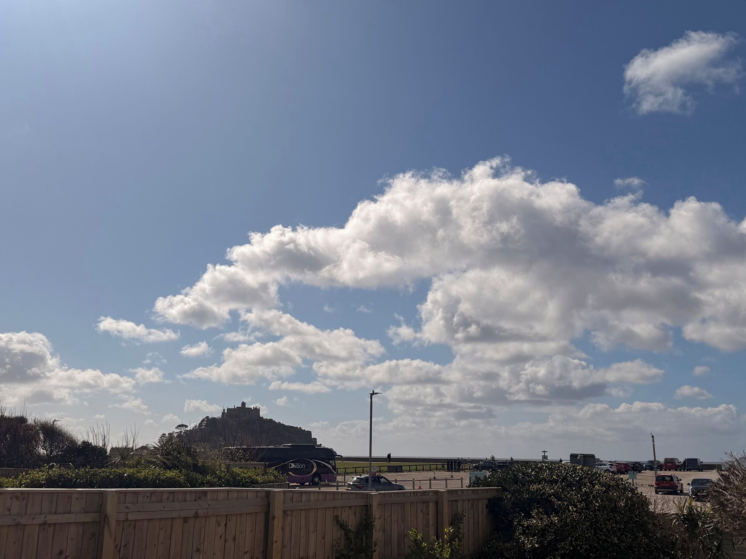 A clear sky with scattered clouds, a distant castle-like structure, and a parked bus.