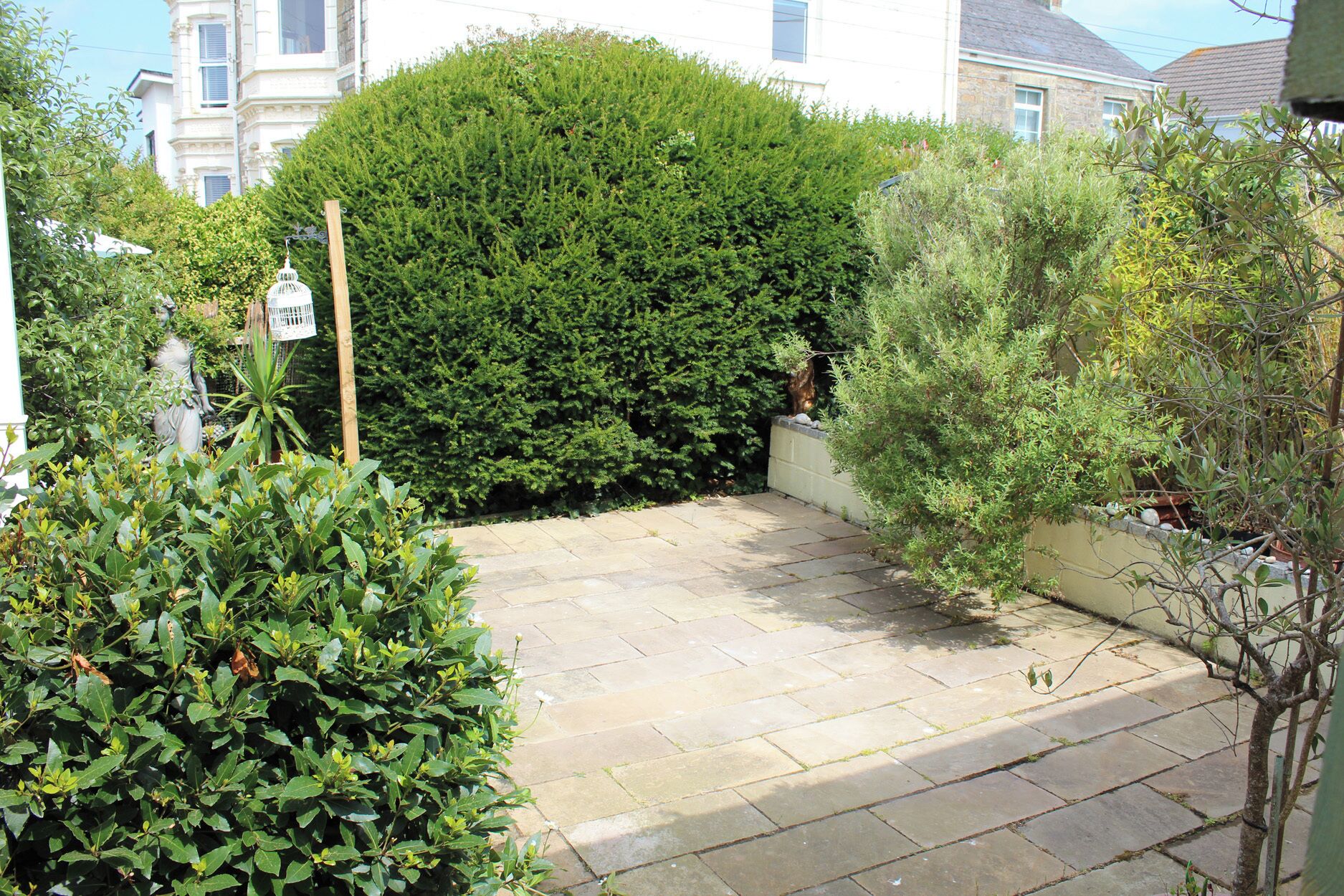 A paved garden area with a variety of plants and a statue.