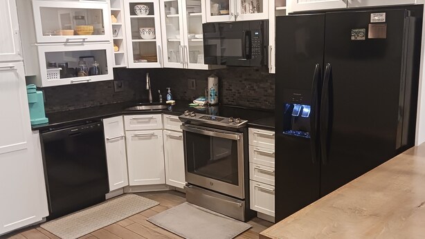 A modern kitchen with white cabinets, a black refrigerator, stainless steel appliances, and a tiled backsplash. - 2-bedroom condo in wonderful Isle of Palms with AC
Beach and Pier access (Isle of Palms)