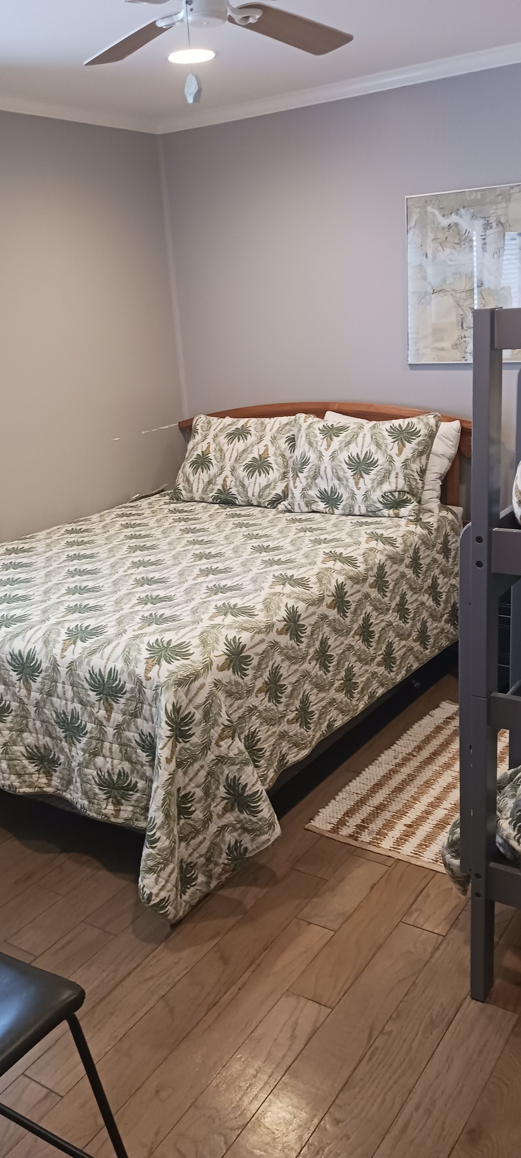 Una camera da letto con un letto, una ventola a soffitto, un pavimento in legno e un'opera d'arte appesa al muro.