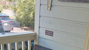 A porch with two wicker chairs with striped cushions, a wooden railing, and a sign prohibiting items on the balcony. - 2-bedroom condo in wonderful Isle of Palms with AC
Beach and Pier access (Isle of Palms)