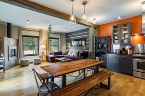 A modern kitchen with a dining area, wooden flooring, and a large window.