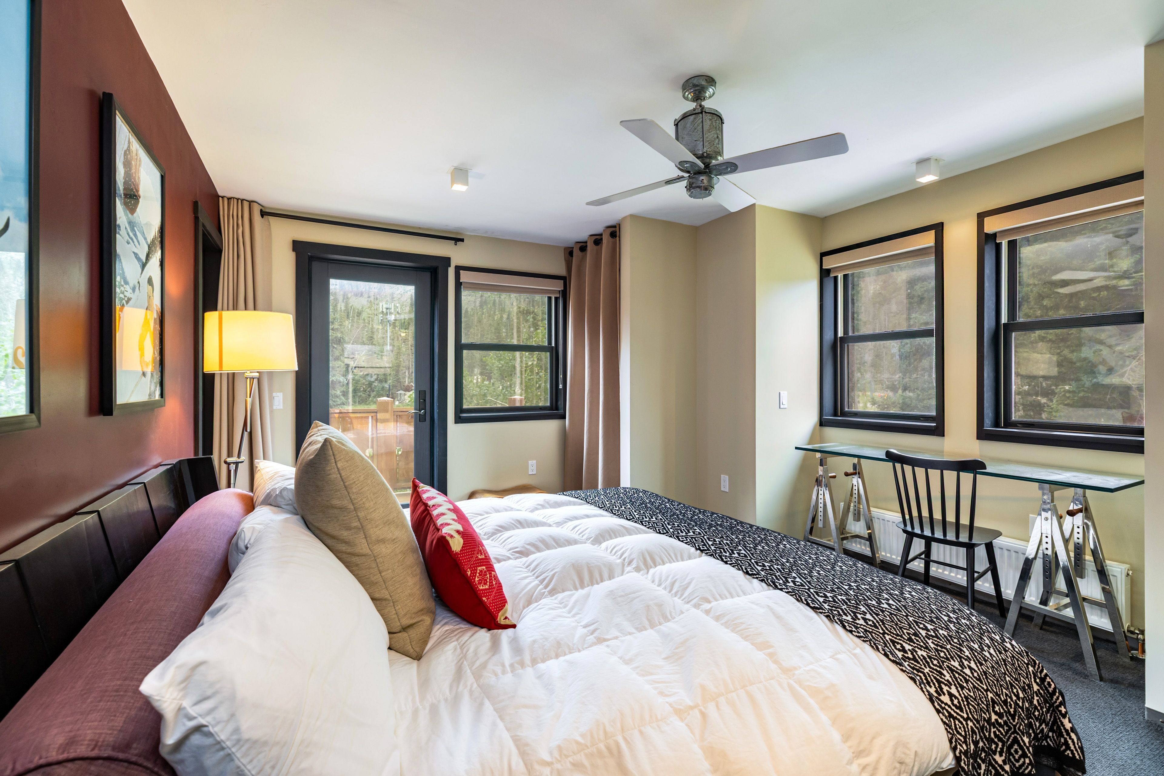 Une chambre d’hôtel équipée d’un lit, d’un bureau, d’une chaise, d’un ventilateur de plafond et de grandes fenêtres.