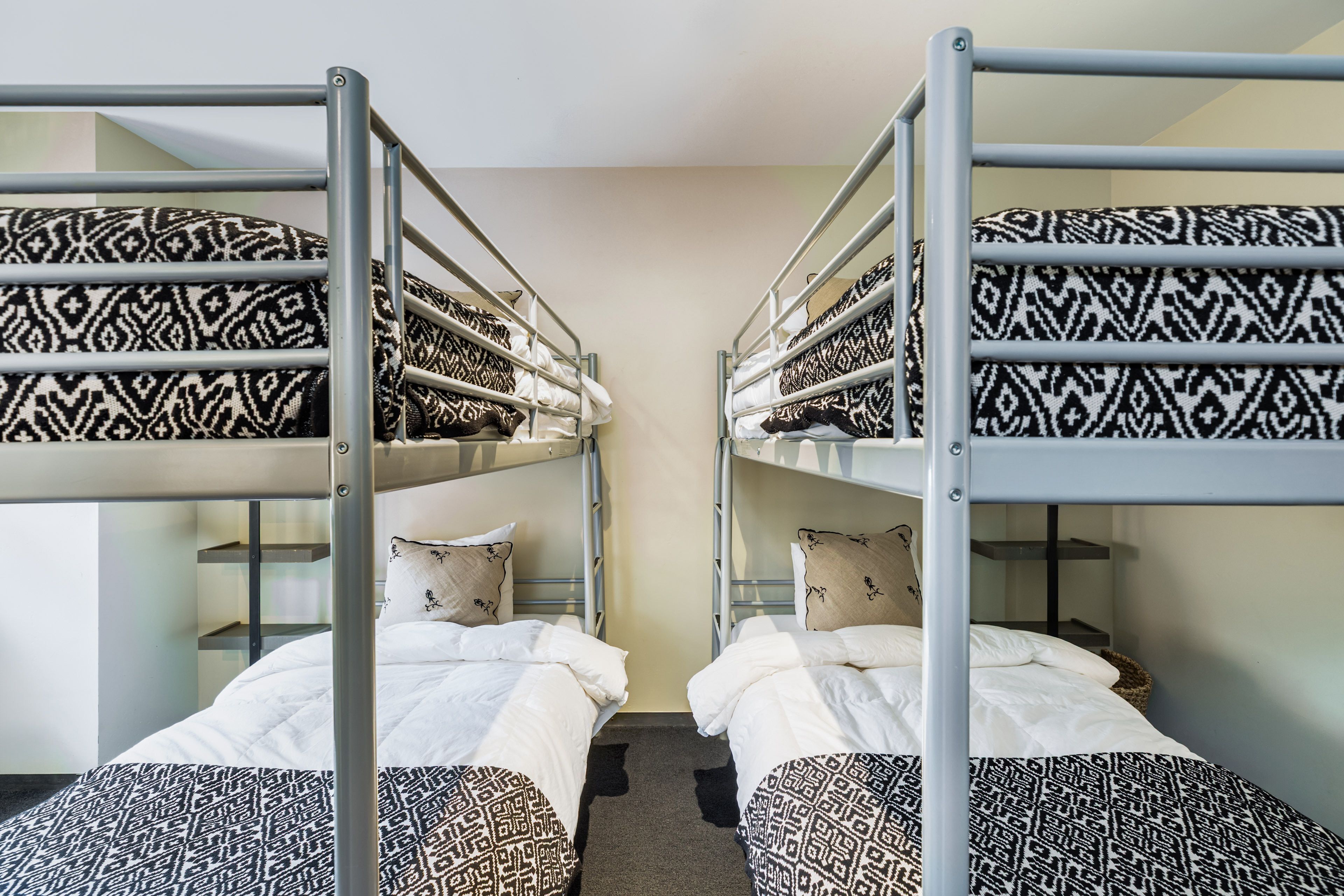 Une chambre avec des lits superposés, chacun agrémenté de draps et d’oreillers à motifs, et un mur aux couleurs neutres.