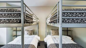 Une chambre avec des lits superposés, chacun agrémenté de draps et d’oreillers à motifs, et un mur aux couleurs neutres.