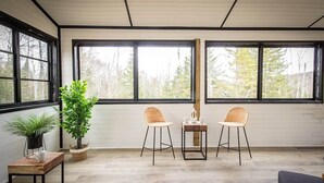 A room with large windows, two chairs, a small table, and a potted plant. - Le Cozy – Hot Tub, Beach & Ski Getaway Tremblant (Lac-Supérieur)