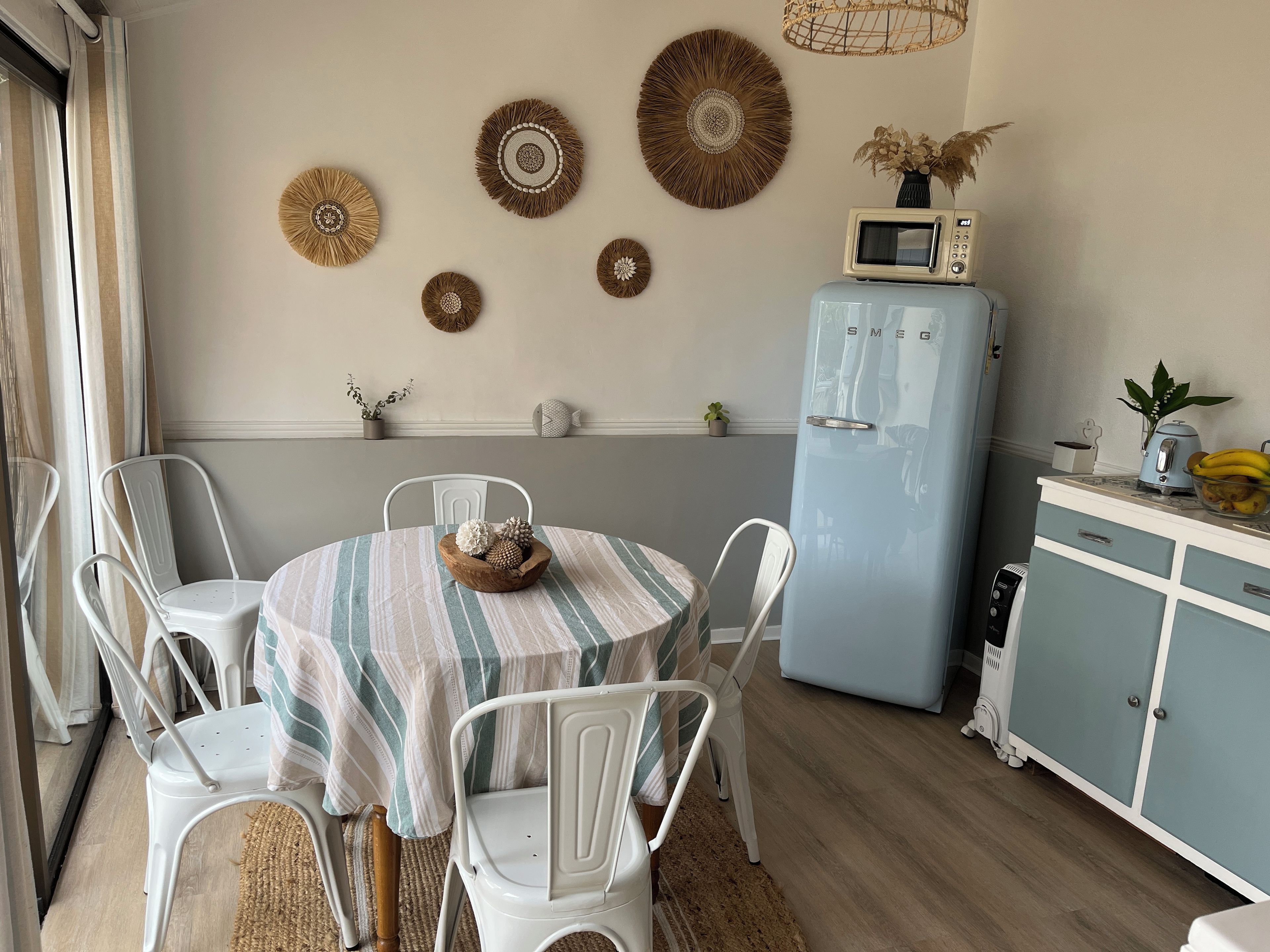A dining area with a round table, white chairs, a striped tablecloth, and a blue refrigerator.