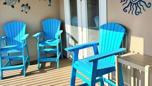 Un’area esterna riparata con poltrone Adirondack blu, un tavolo in legno e decorazioni murali tra cui un sole e creature marine.
