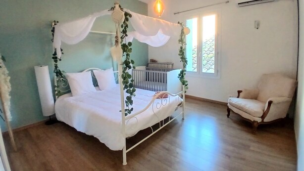 A bedroom with a four-poster bed, a crib, a chair, and a hanging light fixture. - Property XXL 320 m²_10 to 16 pers_Piscine (Roujan)