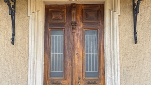 A wooden double door with glass panels, set in a beige stucco wall with decorative moldings and a dark ceiling. - Property XXL 320 m²_10 to 16 pers_Piscine (Roujan)