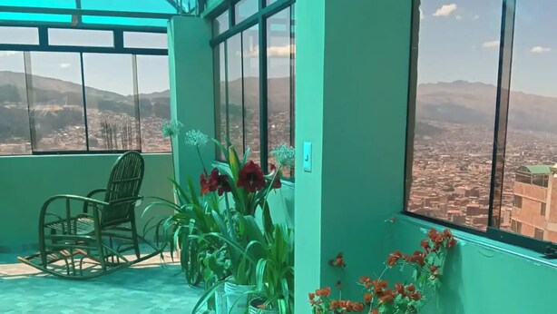 Quarto com vista para a cidade através de grandes janelas, uma cadeira e vários vasos com plantas.