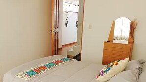 Quarto com cama, cômoda, espelho e TV fixada na parede.