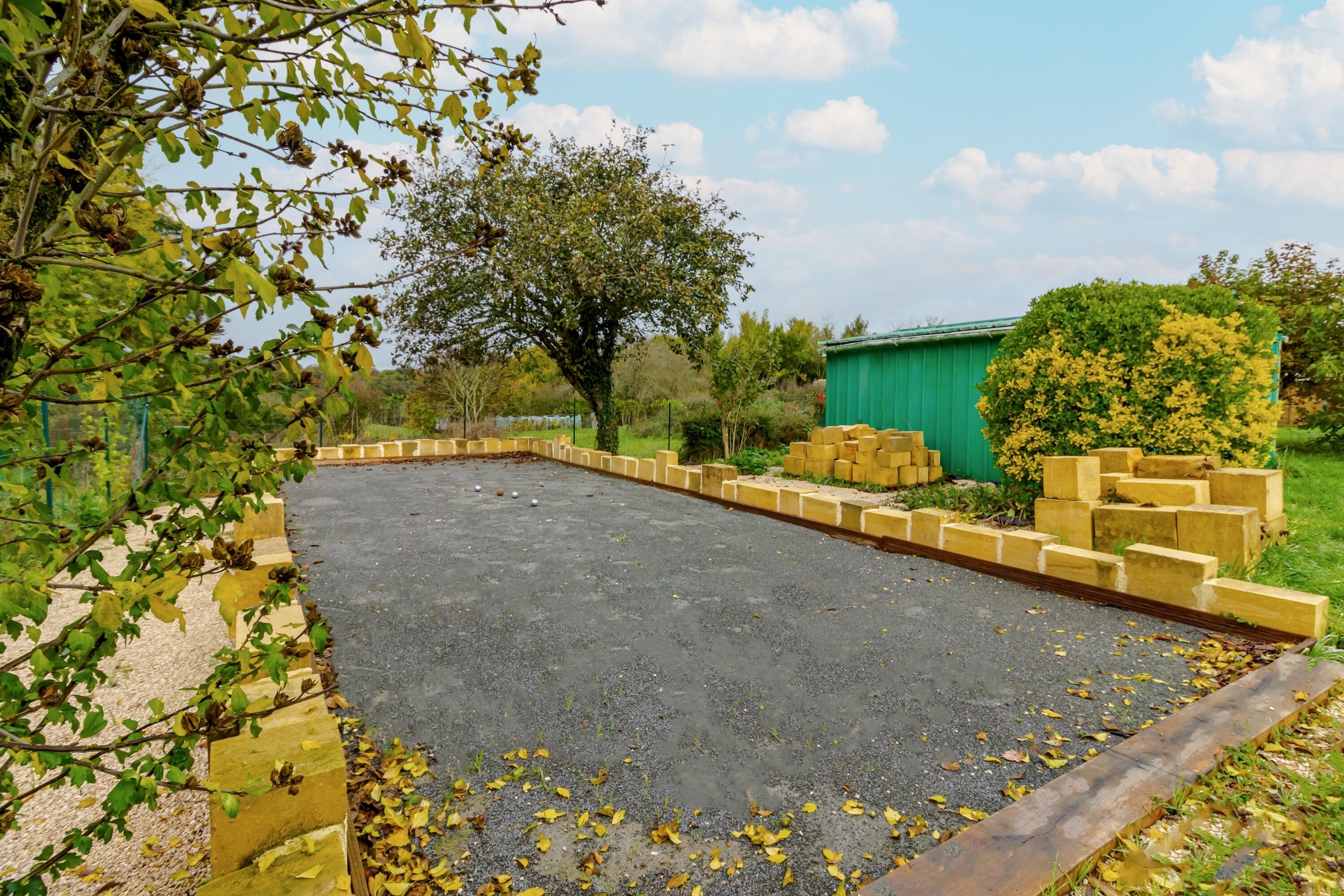 A paved outdoor area with a brick border, surrounded by greenery and a tree.