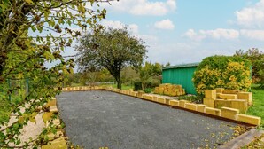 Un espace extérieur aménagé avec un revêtement pavé, bordé de briques, et entouré de verdure et d’un arbre.