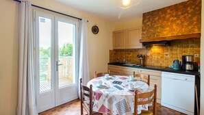 Une cuisine équipée d’une table à manger pour quatre personnes, d’un lave-vaisselle et offrant une vue sur l’extérieur grâce à une porte-fenêtre coulissante.