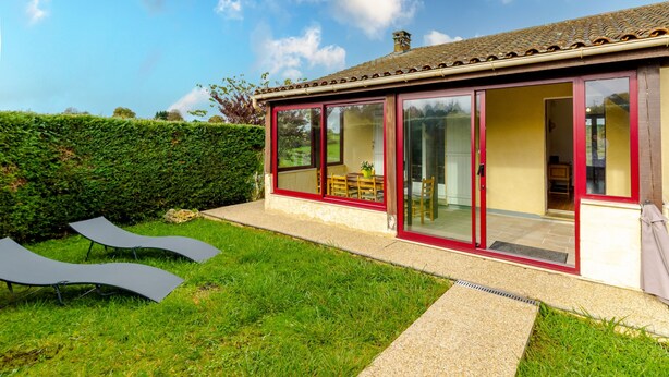 Une maison dotée d’une véranda en verre, d’une pelouse bien entretenue et surplombée d’un ciel dégagé.