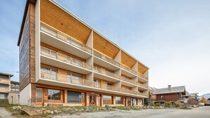 Ett hotell med flera våningar, balkonger, en parkeringsplats och en bergig bakgrund.