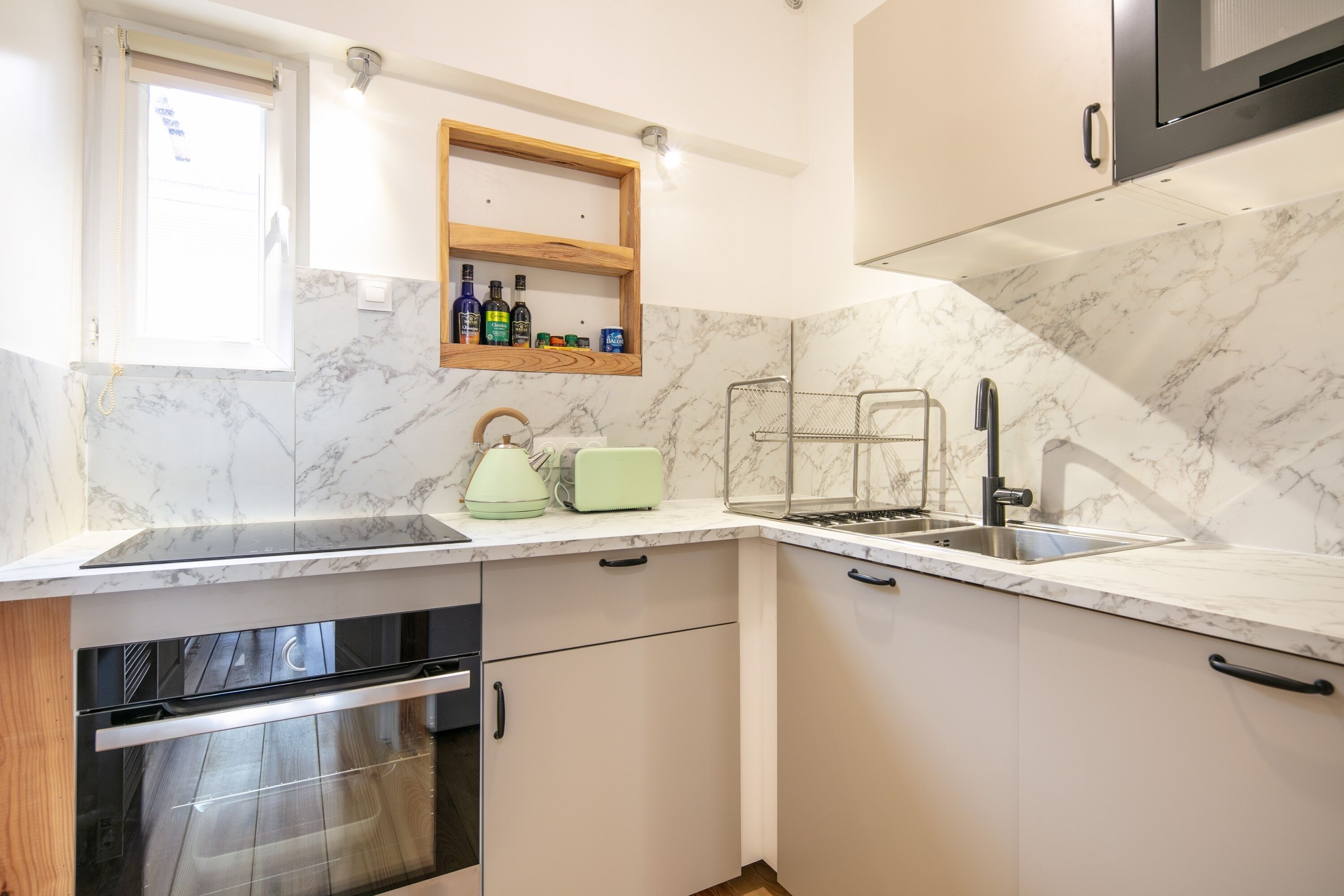 A modern kitchen with a marble backsplash, built-in oven, and a small window.