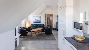 Un appartement moderne de style « loft », avec un espace de vie comprenant un canapé en cuir noir, une table basse en bois et un grand tableau accroché au mur.