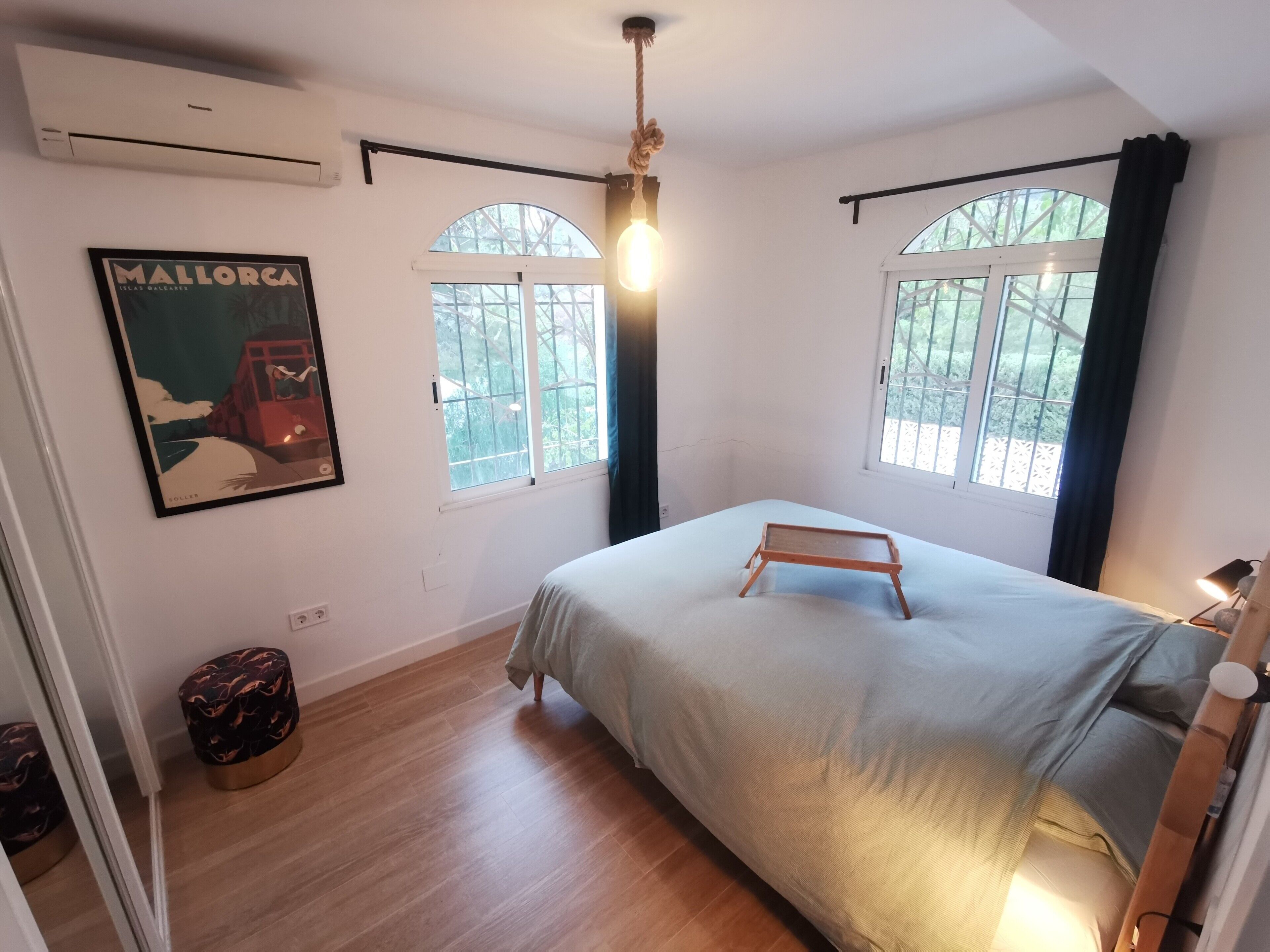 Quarto com cama, duas janelas, um cartaz na parede e uma luminária no teto.