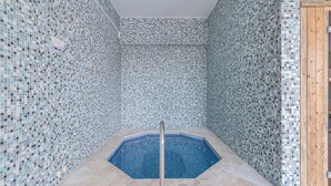 Ett litet, åttkantigt bubbelbad med ett metallräcke runt om, omgivet av väggar klädda med mosaikplattor.