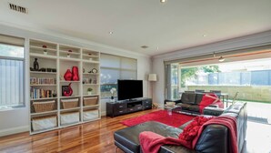 A modern living room with a black leather sofa, a flat-screen TV, and a white shelving unit filled with books and decorative items.