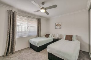 A hotel room with two beds, a ceiling fan, a window with blinds, and a painting on the wall.