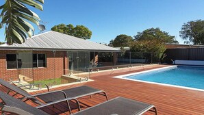 A swimming pool with lounge chairs, a glass-enclosed building, and a brick wall.