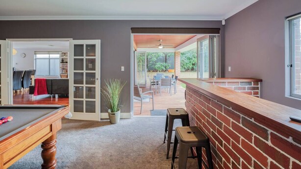 A spacious room with a pool table, a bar area with stools, and a view of an outdoor patio with furniture.
