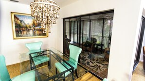 A dining area with a glass table and teal chairs, a chandelier, and a large window with a view of an outdoor patio. - 3-bedroom Jupiter condo in gated community (Jupiter)